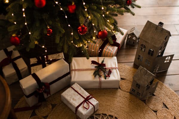 Christmas gift boxes on wooden floor under xmas tree at home. Winter holiday season.